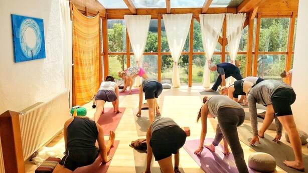 A yoga class in a room with large windows, wooden beams, and exercise mats.