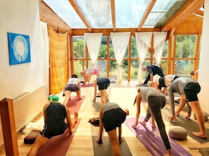 A yoga class in a room with large windows, wooden beams, and exercise mats.