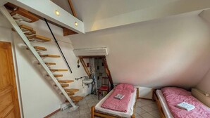 Una habitación con escaleras de madera, un baño pequeño y dos camas individuales con ropa de cama a cuadros.