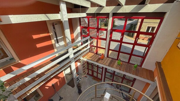 A multi-level building with a red-framed window, a balcony, and a staircase.