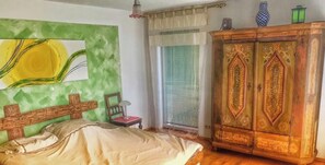 A bedroom with a bed, a wooden cabinet, a chair, a lamp, and a window with curtains.