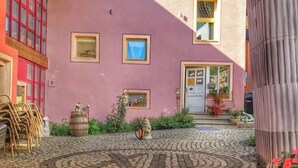 A pink building with a covered patio, a wooden door, and a small garden area.