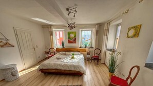 Ein Schlafzimmer mit einem großen Bett, Nachttischen, einem Sessel, einer Pendelleuchte und einem Fenster mit Vorhängen.