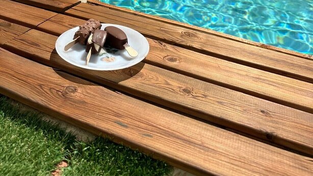 Uma piscina com água cristalina, um deck de madeira e um prato com doces de chocolate.