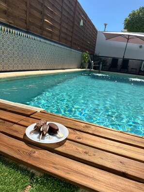 A swimming pool with clear water, a wooden deck, and a plate with chocolate-covered treats. - Holiday Home 'Gení' with Private Pool, Wi-Fi, and Air Conditioning (la victoria)