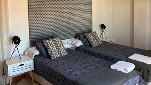 Quarto de hotel com duas camas, cabeceira, abajures, mesas de cabeceira e ar condicionado fixado na parede.