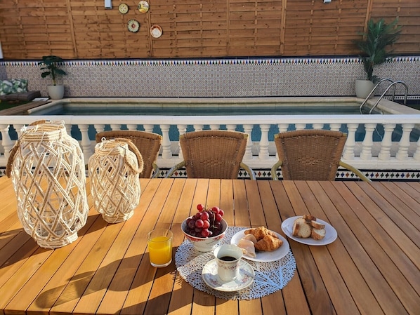 A wooden table with wicker chairs, a glass of orange juice, a bowl of grapes, a plate of croissants, and a cup of coffee.