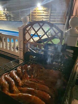 A grill with sausages being cooked, a wooden lattice structure, and a white railing.