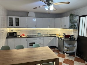 A kitchen with white cabinets, a microwave, a sink, a wooden table, and a ceiling fan.