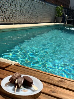 A swimming pool with clear water, a wooden deck, and a plate with chocolate-covered treats.