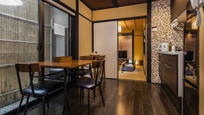 Una cucina moderna con pavimento in legno scuro, un'area pranzo con tavolo e sedie in legno e vista su un muro di mattoni attraverso una finestra.