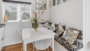 A modern kitchen with white cabinetry, a white dining table, and a patterned sofa. - Stylish Waterfront Studio Sanctuary! (Ngunguru)