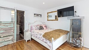 A bedroom with a white bed, a television mounted on the wall, a cabinet, and a mirror. - Stylish Waterfront Studio Sanctuary! (Ngunguru)