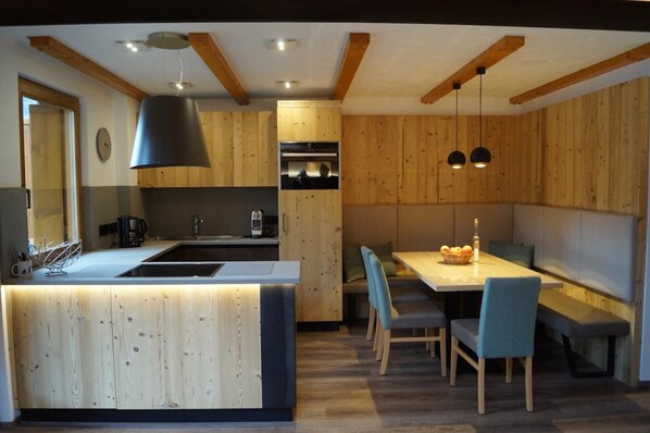 A modern kitchen with wooden cabinetry, a central island, and pendant lighting. - Bucaneve - Lake View Apartment in Predazzo (Predazzo)