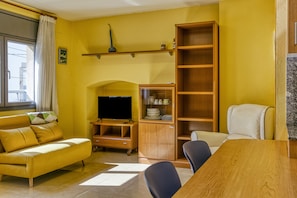 A yellow-walled room with a sofa, a TV stand, a wooden cabinet, and a dining table.