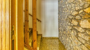 Un escalier avec des rampes en bois menant à une pièce dont un des murs est en pierre et qui est éclairée par un luminaire au plafond.