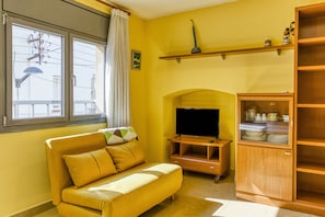 A living room with a sofa, television, wooden cabinet, and a window with curtains.