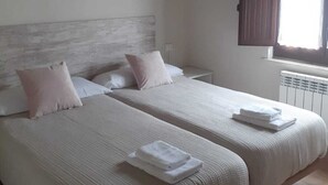 A room with two beds, wooden beams on the ceiling, a window with curtains, and a white radiator. - Impeccable 3-Bed House in Cangas de Onis (Cangas de Onis)
