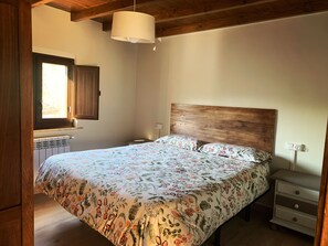 Un dormitorio con cabecera de madera, cama con ropa de cama floral, mesita de noche y ventana con vistas.