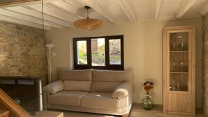 A living room with a beige sofa, a wooden cabinet with glass doors, a stone wall, and a window with a view of a garden. - Impeccable 3-Bed House in Cangas de Onis (Cangas de Onis)