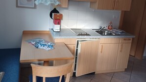 Una cucina compatta con mobili in legno, lavastoviglie integrata, lavello e un piccolo tavolo da pranzo con una sedia.