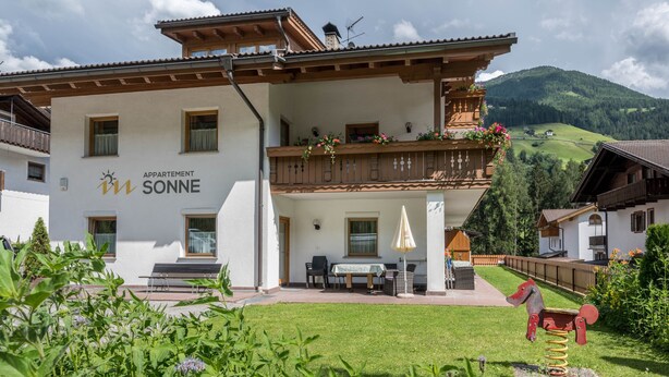 Un edificio a due piani con un balcone, una sala da pranzo e un’area giochi con un’altalena a forma di cavallo.