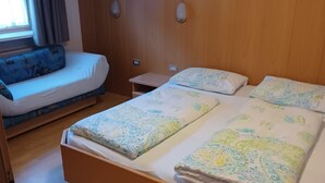 Una camera d'hotel con un letto di legno, una poltrona, una finestra con tende e un punto luce fissato alla parete.