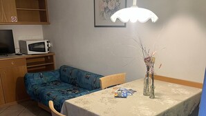 Ein Essbereich mit Tisch, Stühlen, einer Mikrowelle, einem Sofa und einem Wandbild.