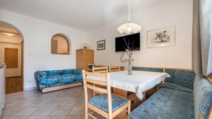 Ein Zimmer mit Esstisch, zwei blau gemusterte Sofas, einem Holzschrank, einem Fernseher und einem gerahmten Bild an der Wand.