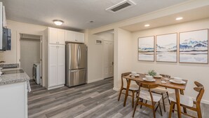 A modern kitchen with white cabinets, a stainless steel refrigerator, and a dining area with a wooden table and chairs. - Cheerful 1-Bedroom with free parking (Reno)