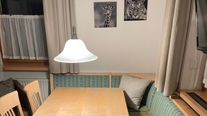 Una habitación con una mesa de comedor de madera, dos sillas, un sofá con cojines, una pequeña mesa redonda con una revista y dos cuadros en la pared.