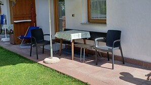 Un patio al aire libre con una mesa, sillas, un paraguas blanco y una puerta de madera.