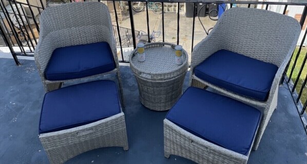 Two wicker chairs with blue cushions and a small round table with two bottles on a balcony.