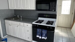 Una cocina con armarios blancos, un microondas negro, una estufa y un lavamanos.
