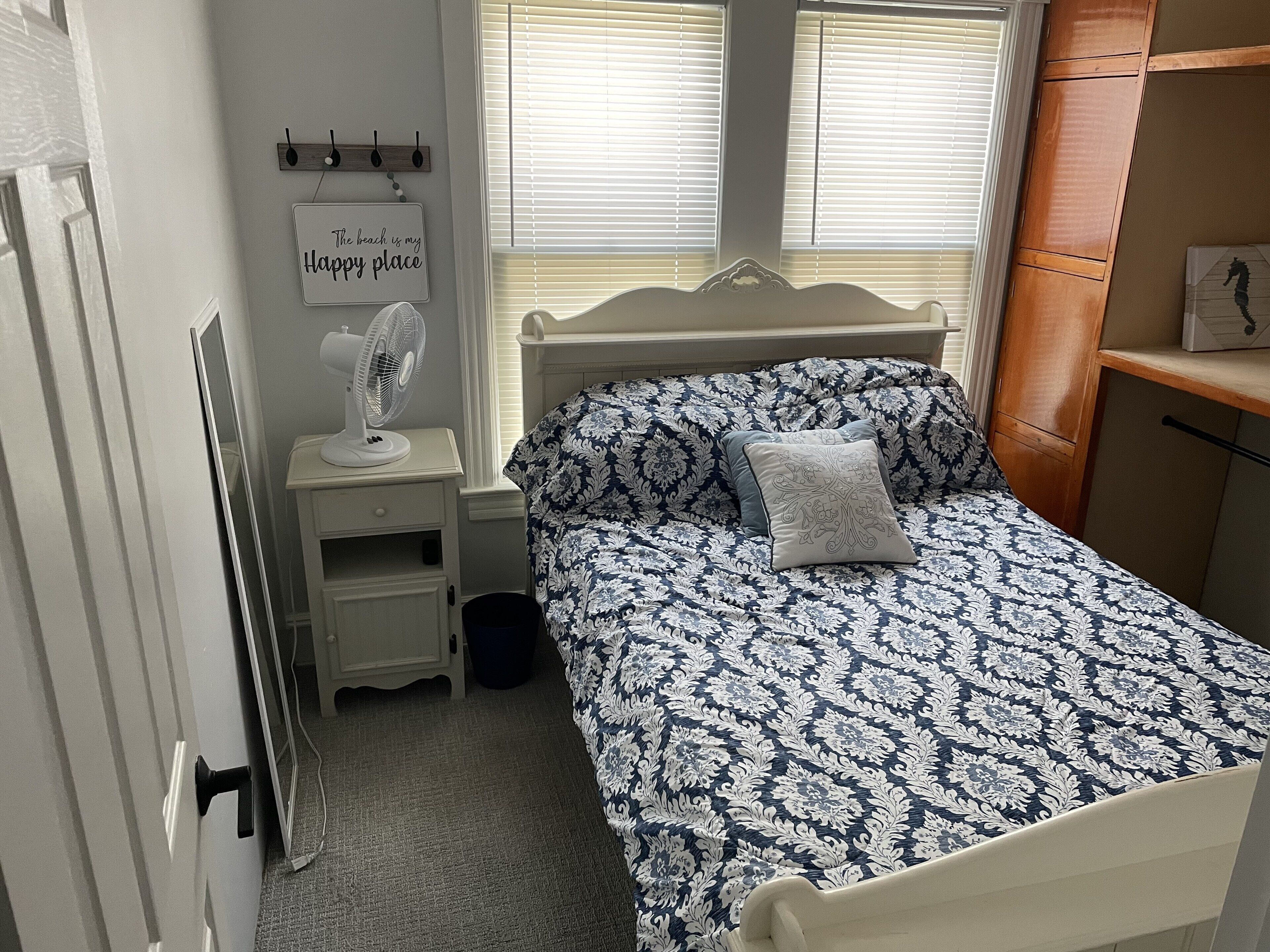 A bedroom with a bed, bedside table, and a wall-mounted fan.