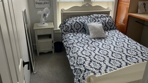 Un dormitorio con cama, mesita de noche y ventilador de pared.