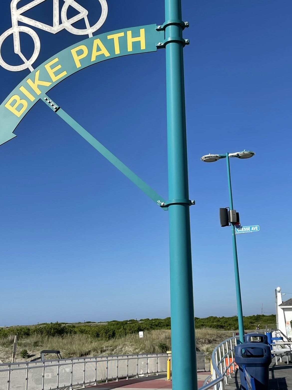 Ein Fahrradwegweiser mit einem Fahrradsymbol und der Aufschrift 'BIKE PATH' an einem türkisblauen Pfosten.
