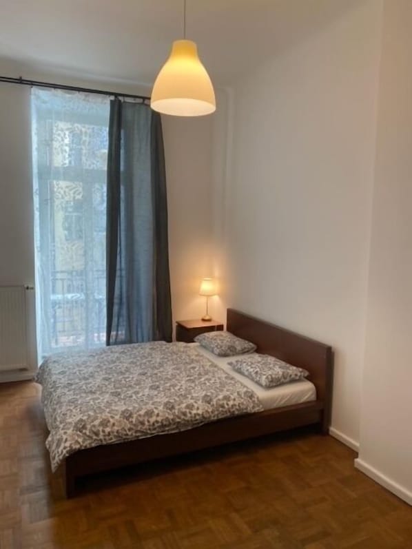 A bedroom with a bed, a nightstand, a lamp, and a window with curtains. - 3 Bed Flat - Sleeps 10 - Pets - Smoking on terrace (Praha)