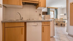 Eine Küche mit Holzausstattung, einem Geschirrspüler von Bosch, einer Arbeitsplatte aus Granit und einem Essbereich mit Tisch und Stühlen.