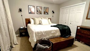 Un dormitorio con una cama, un ventilador de techo, una mesita de noche, una lámpara, un aparador y una cesta.
