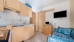 Una cocina compacta con gabinetes de madera, microondas y televisión.