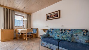 Una sala de estar con sofá, una mesa de comedor con sillas, una zona de cocina y un ventanal con cortinas.