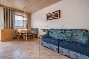 Un salon avec un canapé, une table à manger avec des chaises, un coin cuisine et une fenêtre avec des rideaux.