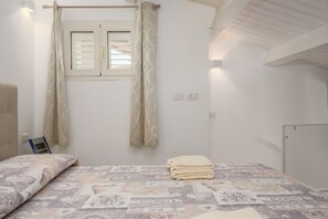 Un dormitorio con cama, una ventana con cortinas, una mesita de noche y una lámpara de pared.