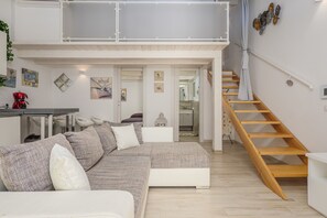 Un moderno espacio tipo loft con techo alto, una escalera de madera y un área de comedor con una cafetera roja.