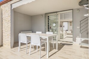 Un patio al aire libre con una mesa y sillas, un vidrio que da a un balcón y una escalera.