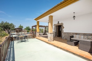 Un patio exterior con una pérgola, zona de estar y un muro de piedra.