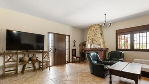 Una sala de estar con televisión, sillones de cuero, chimenea de piedra y piso de baldosas.