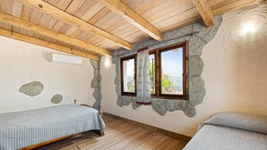 Una habitación con techo de madera, pared de piedra, ventana con cortinas y cama con edredón acolchado.