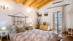 Een slaapkamer met een bed, nachtkastjes, een dressoir, een hangplant, een raam met gordijnen en een balkon.